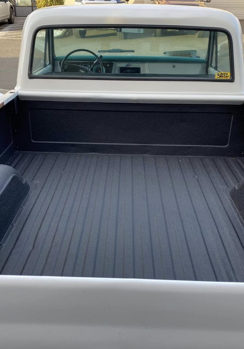 View of an empty white pickup truck bed with a black liner, seen from the back tailgate; several parked cars are visible in the background, highlighting the durability of protective coatings Auburn WA drivers trust.
