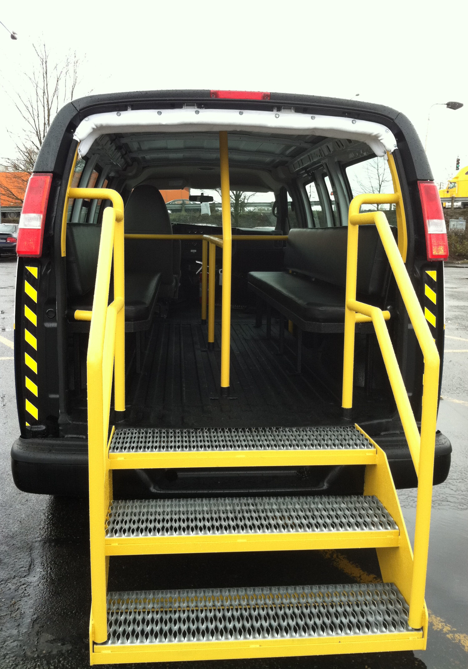 A black van with yellow handrails and steps leading into the interior, featuring bench seating along the sides and durable spray-on truck bed liners Auburn for added protection.