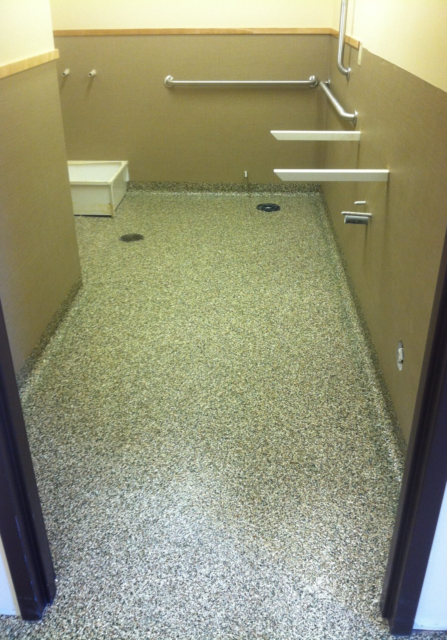 A restroom with grab bars and missing fixtures features a speckled floor, possibly finished with industrial floor coatings Auburn WA; both the toilet and sink are absent.