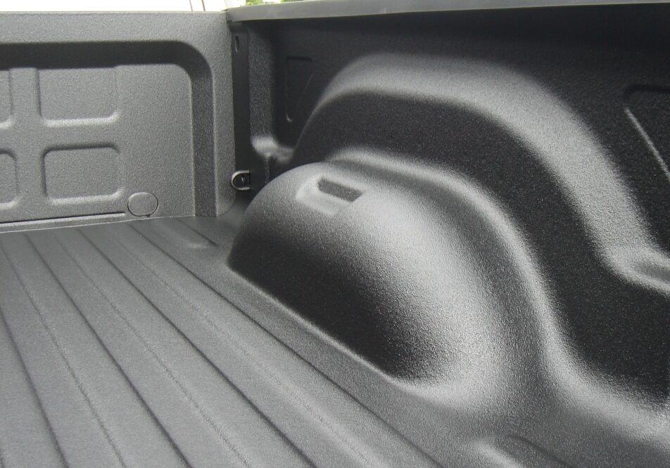 The image shows the inside of a pickup truck bed with a black, textured spray-on liner coating the surface, similar to those discussed in Rhino Linings of Auburn FAQs.