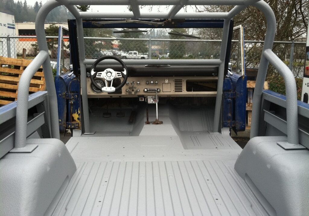 The interior of a stripped-down, partially restored vehicle with no seats, exposed metal floor, and a steering wheel installed—perfect for discussing Rhino Linings of Auburn FAQs on durable floor coating solutions.