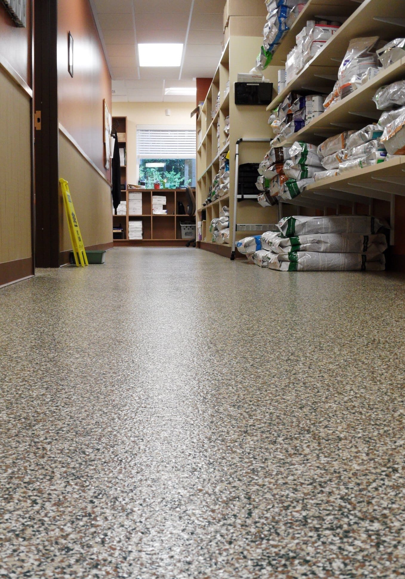A hallway in a store or veterinary clinic features durable residential and commercial flooring Auburn WA, with shelves of pet food and supplies on the right and a yellow caution sign visible in the distance.