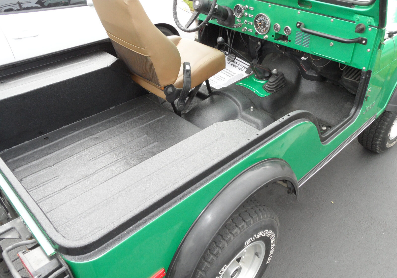 Green vintage Jeep with missing passenger seat, exposing the bare metal floor and interior—an ideal candidate for protective coatings in Western Washington. Dashboard, steering wheel, and gear shift remain visible.