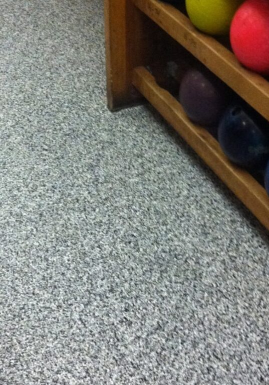 Bowling balls of various colors with protective coatings are stored on a wooden rack next to a speckled-pattern floor in Western Washington.